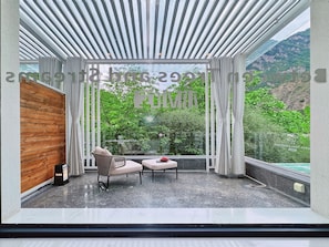 A balcony with a view of a mountainous landscape, a wooden panel wall, a wicker chair, a small table, and a sign. - Between Trees and Streams (Ngawa Autonomous Prefecture)