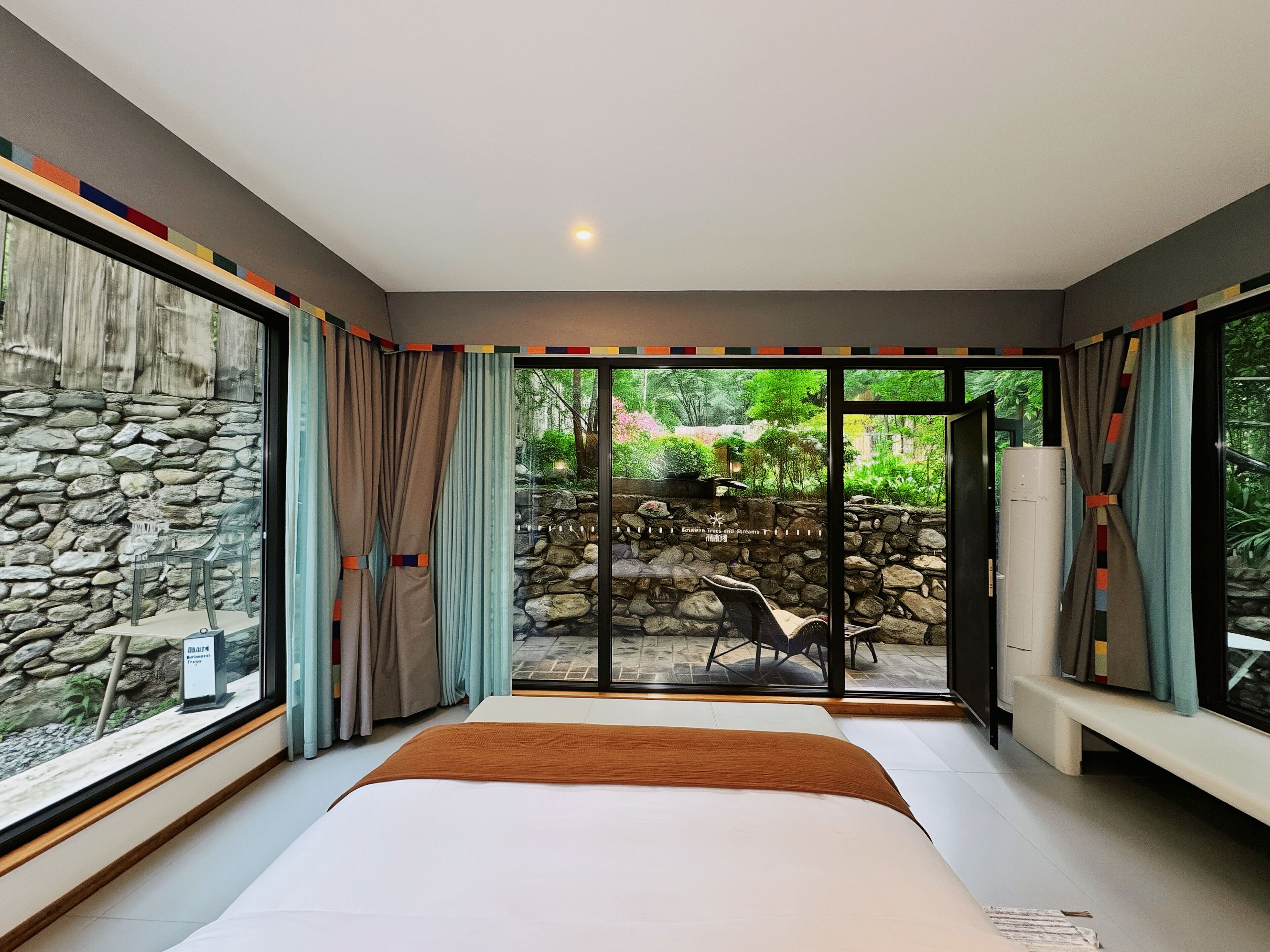 A bedroom with a large bed, a stone wall, and a view of an outdoor garden.
