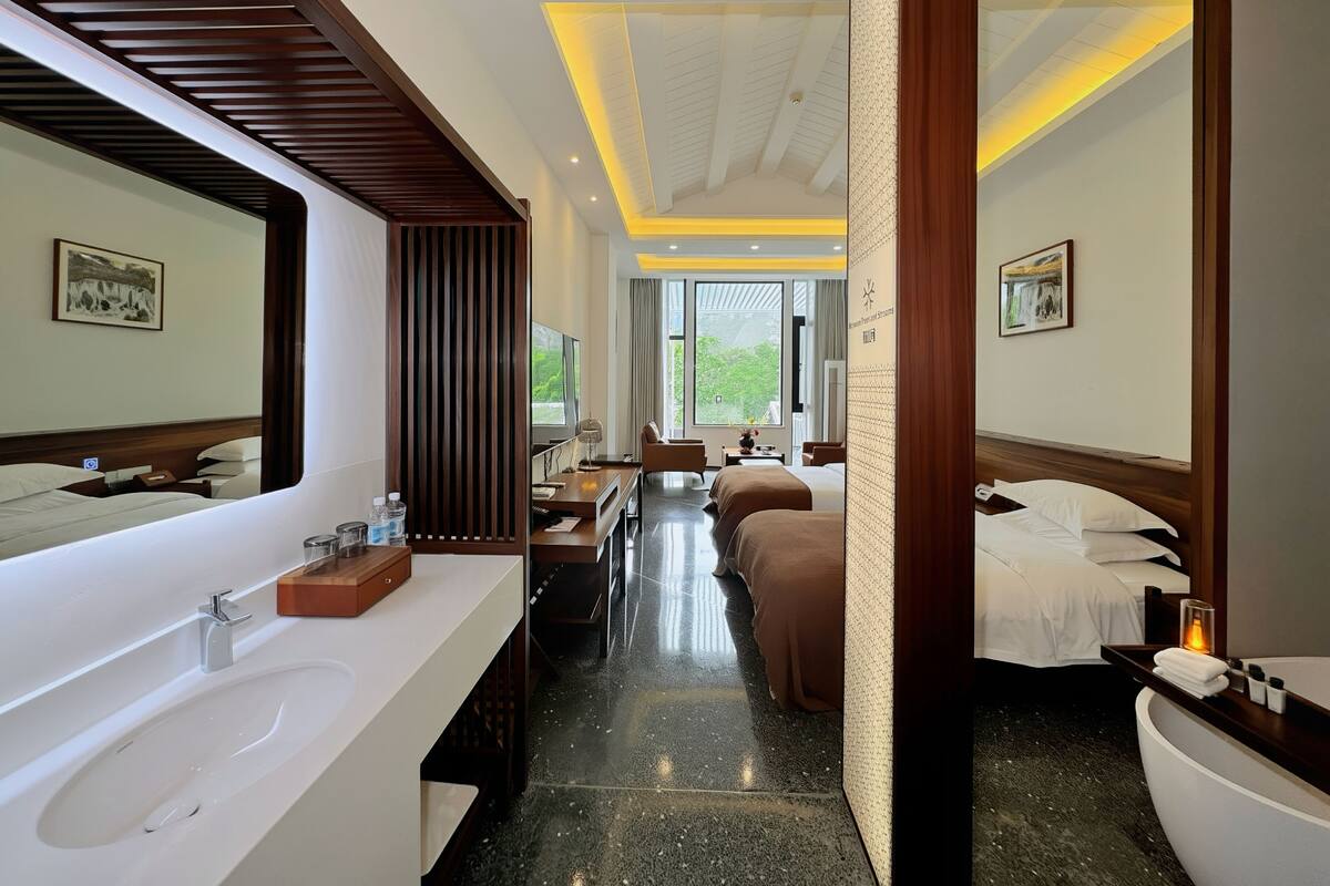 A hotel room with a large mirror, a double bed, a sofa, a desk, and a bathroom with a sink and mirror.