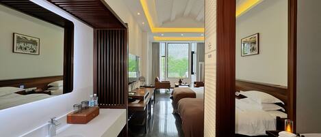 A hotel room with a large mirror, a double bed, a sofa, a desk, and a bathroom with a sink and mirror.