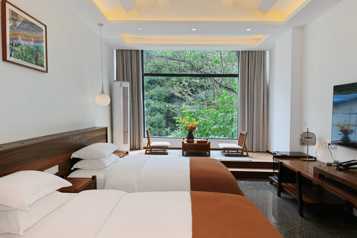 A hotel room with a large window, a bed, a desk, and a chair.