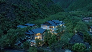 Een modern huis met meerdere niveaus, omgeven door weelderige begroeiing en heuvels.