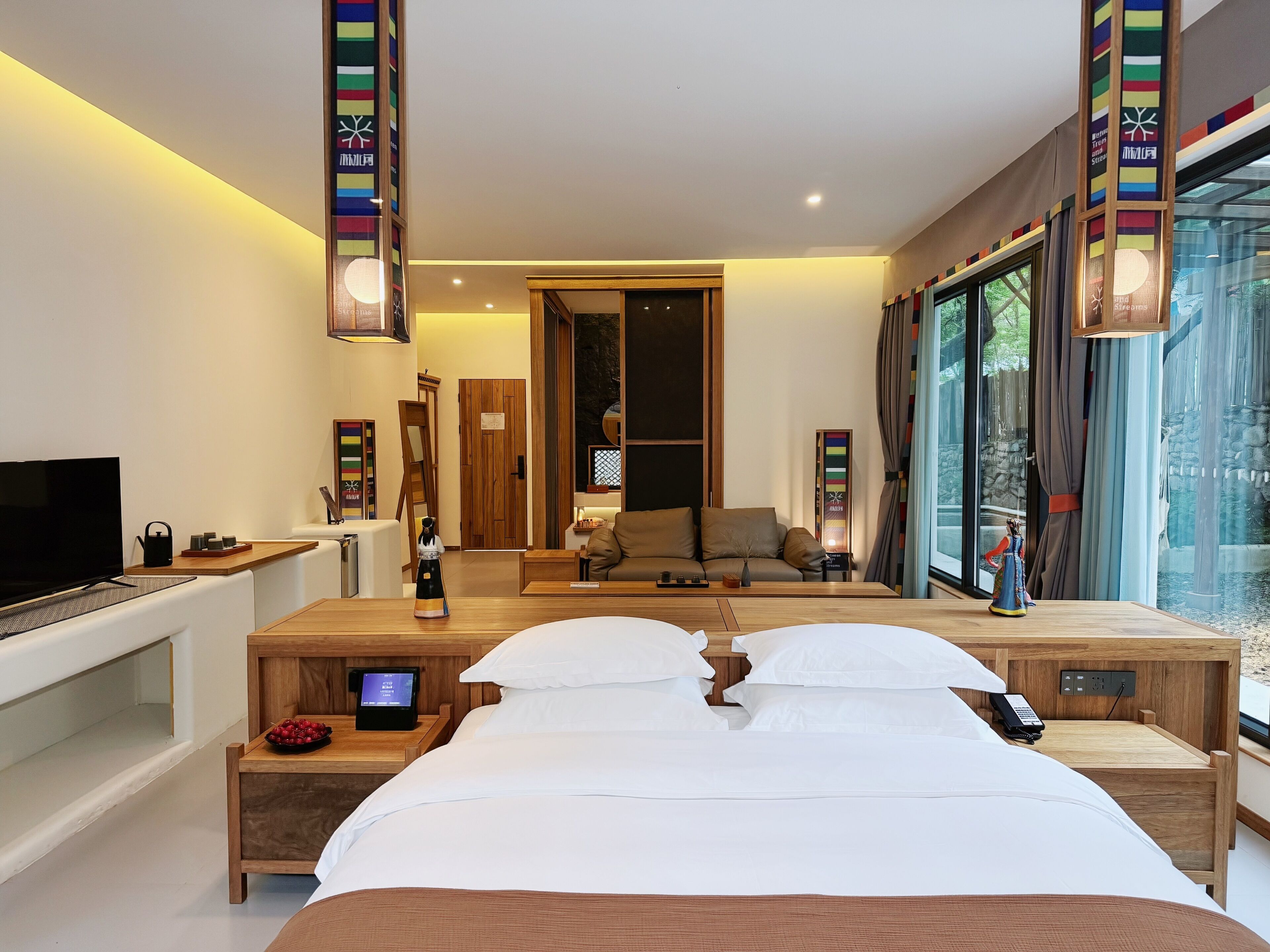 A modern hotel room with a large bed, bedside tables, a TV, and a view of the outdoors.