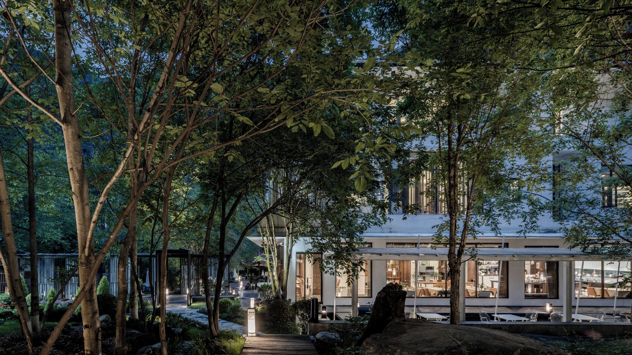 A modern building with a glass facade, surrounded by trees and a pathway.