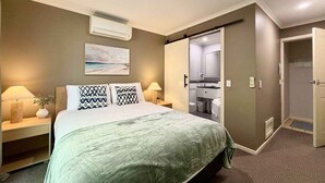 A bedroom with a bed, bedside tables, a mirror, and a door leading to a bathroom. - Splash at Sapphire - Pet Friendly, Resort Pool, Beachfront (Coffs Harbour)