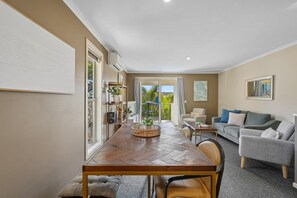 A dining area with a wooden table, chairs, and a view of the outdoors through a glass door. - Splash at Sapphire - Pet Friendly, Resort Pool, Beachfront (Coffs Harbour)