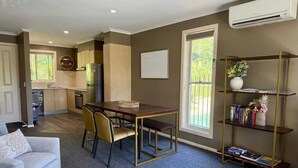 A modern living room with a dining area, a sofa, a coffee table, and a bookshelf. - Splash at Sapphire - Pet Friendly, Resort Pool, Beachfront (Coffs Harbour)