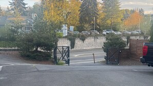 Un espace de stationnement doté d’une entrée fermée par un portail, d’un mur en briques et d’arbres en arrière-plan.