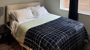 Une chambre à coucher avec un lit, une fenêtre avec des rideaux, un luminaire au plafond et une table de chevet.