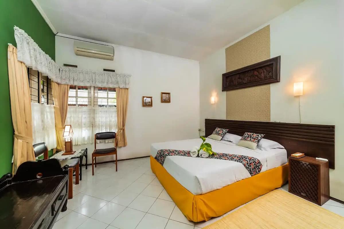A hotel room with a bed, a desk, a chair, a lamp, and a wall-mounted air conditioner.