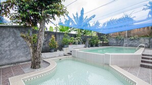 A swimming pool with tiled edges, surrounded by potted plants and a tree. - Dedaunan Guesthouse (Batu)