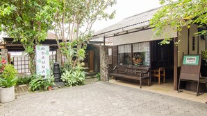 A courtyard with a hexagonal tiled floor, a wooden bench, a stone pillar, and a sign indicating a gallery. - Dedaunan Guesthouse (Batu)