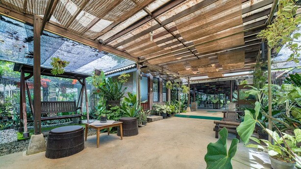 A covered outdoor area with seating, potted plants, and a view of a restaurant. - Dedaunan Guesthouse (Batu)