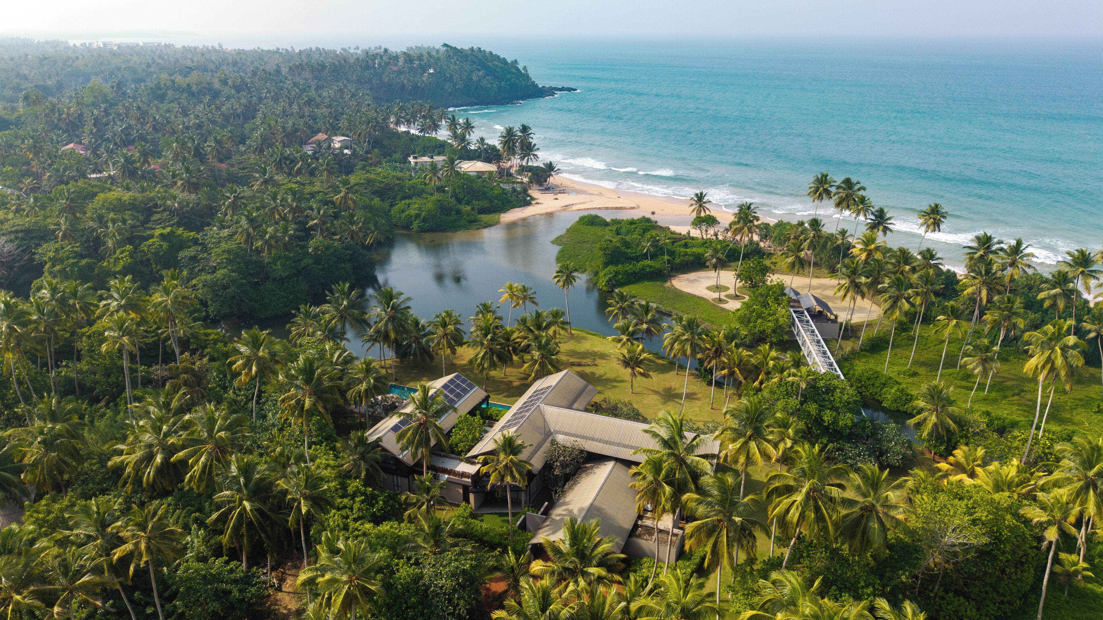 Vista aérea de un resort con playa, palmeras y un lago.