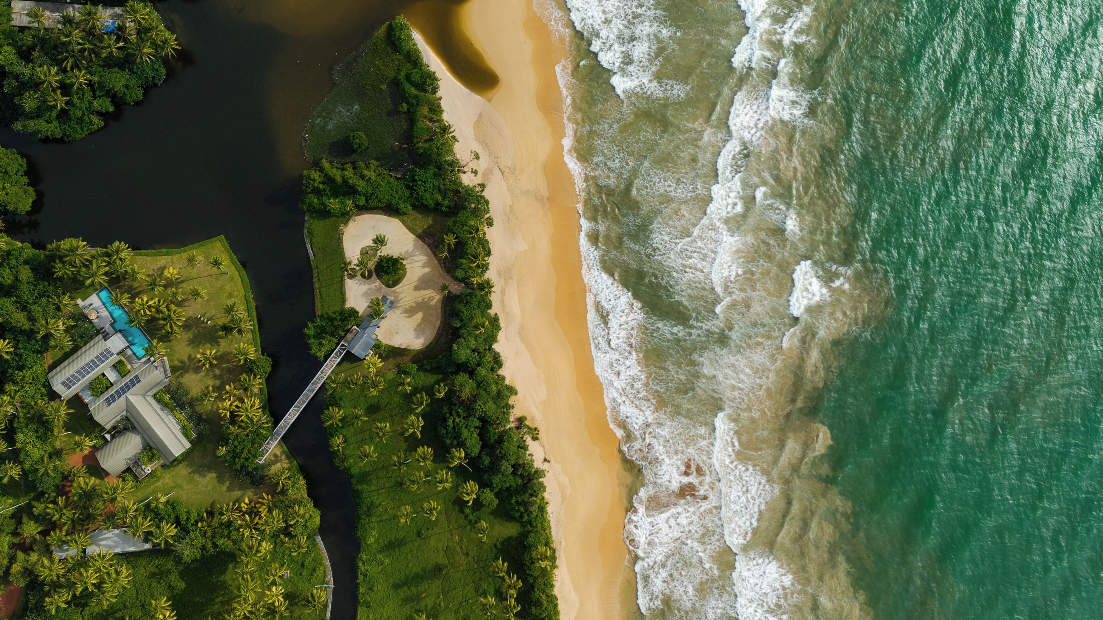 Vista aérea de una propiedad costera con playa, un puente y una piscina.