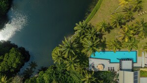 Vista aérea de un complejo turístico con piscina, palmeras y una masa de agua.