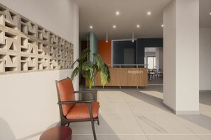 Zona de recepción con mostrador de madera, planta en maceta y área de estar con una silla y una mesa.