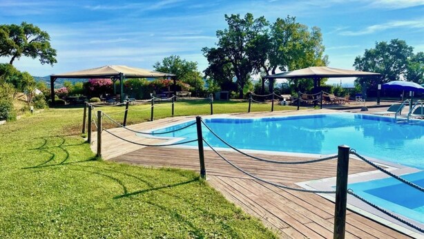 Ein Pool mit Holzterrasse, umgeben von Bäumen und überdachten Sitzbereichen.