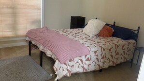 Un dormitorio con cama, mesita de noche, cómoda y ventana con persianas.