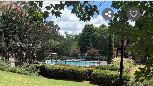 Una piscina rodeada de setos y árboles bien cuidados, con un cielo despejado.