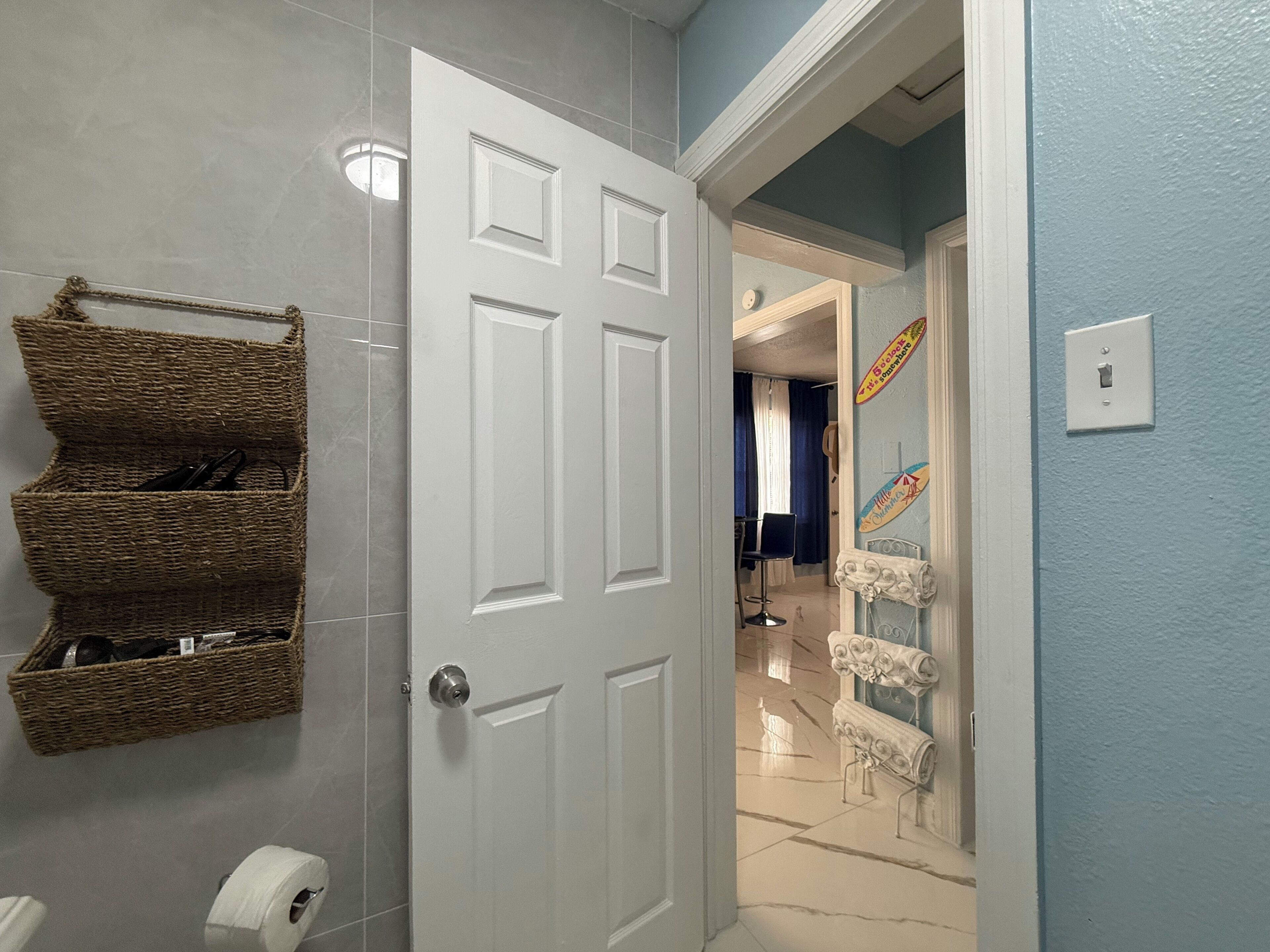 Une salle de bain avec une porte blanche, un panier en osier et un rouleau de papier toilette.