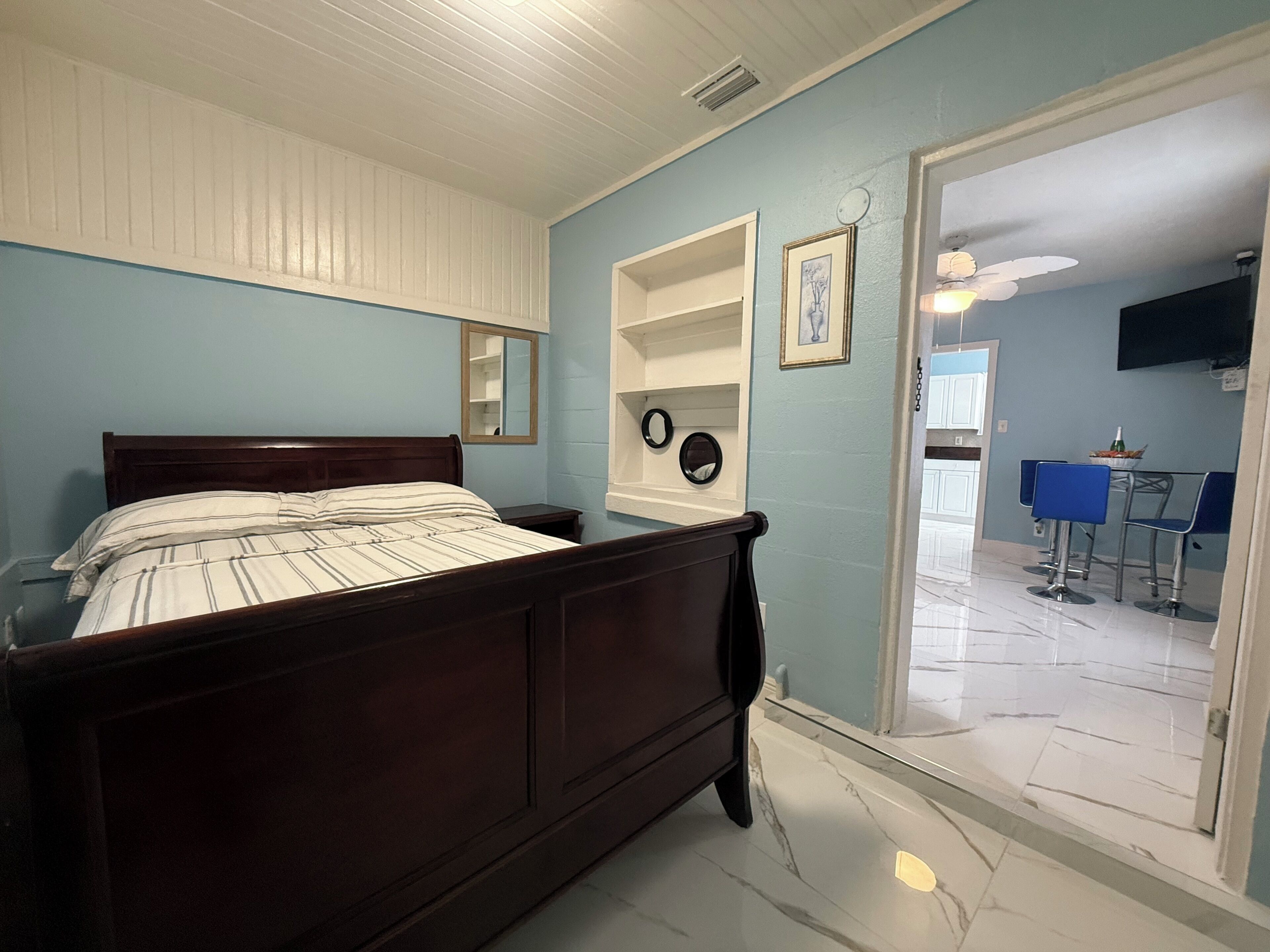 Ein Schlafzimmer mit einem hölzernen Bett, einer weißen Decke, einer blauen Wand und einer Tür zu einem Essbereich.