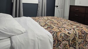 Un dormitorio con cama, ventana con cortinas, puerta y cómoda.