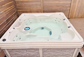 Un bain à remous à l’extérieur en pierre, intégré à une terrasse en bois, avec un mur en bois en arrière-plan.