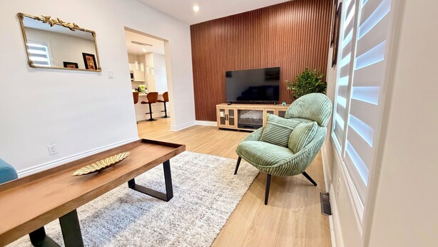 Un salon moderne avec un meuble de rangement en bois pour l’équipement audiovisuel, un fauteuil vert à revêtement en tissu, une table basse en bois et un grand téléviseur à écran plat.