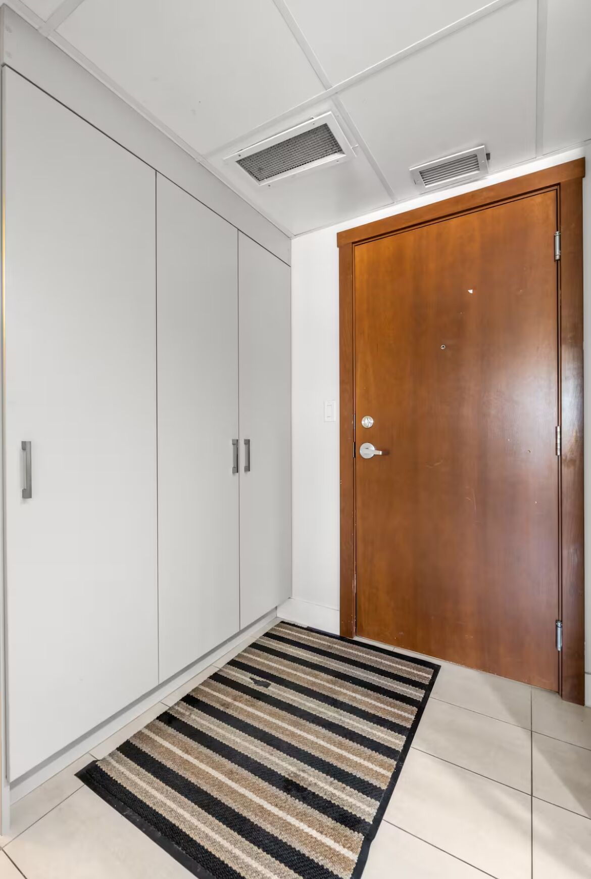 A hallway with a wooden door, white wardrobe, and a striped rug.