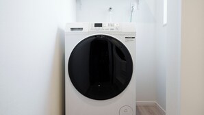 A front-loading white washer and dryer unit with a control panel, placed in a corner with a wooden floor and white walls. - 【5BR Luxury Living】 130㎡DesignerHouse-5BR Luxury Living, Family Roppongi Akasaka (Tokyo)