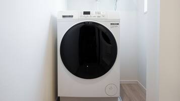 A front-loading white washer and dryer unit with a control panel, placed in a corner with a wooden floor and white walls.