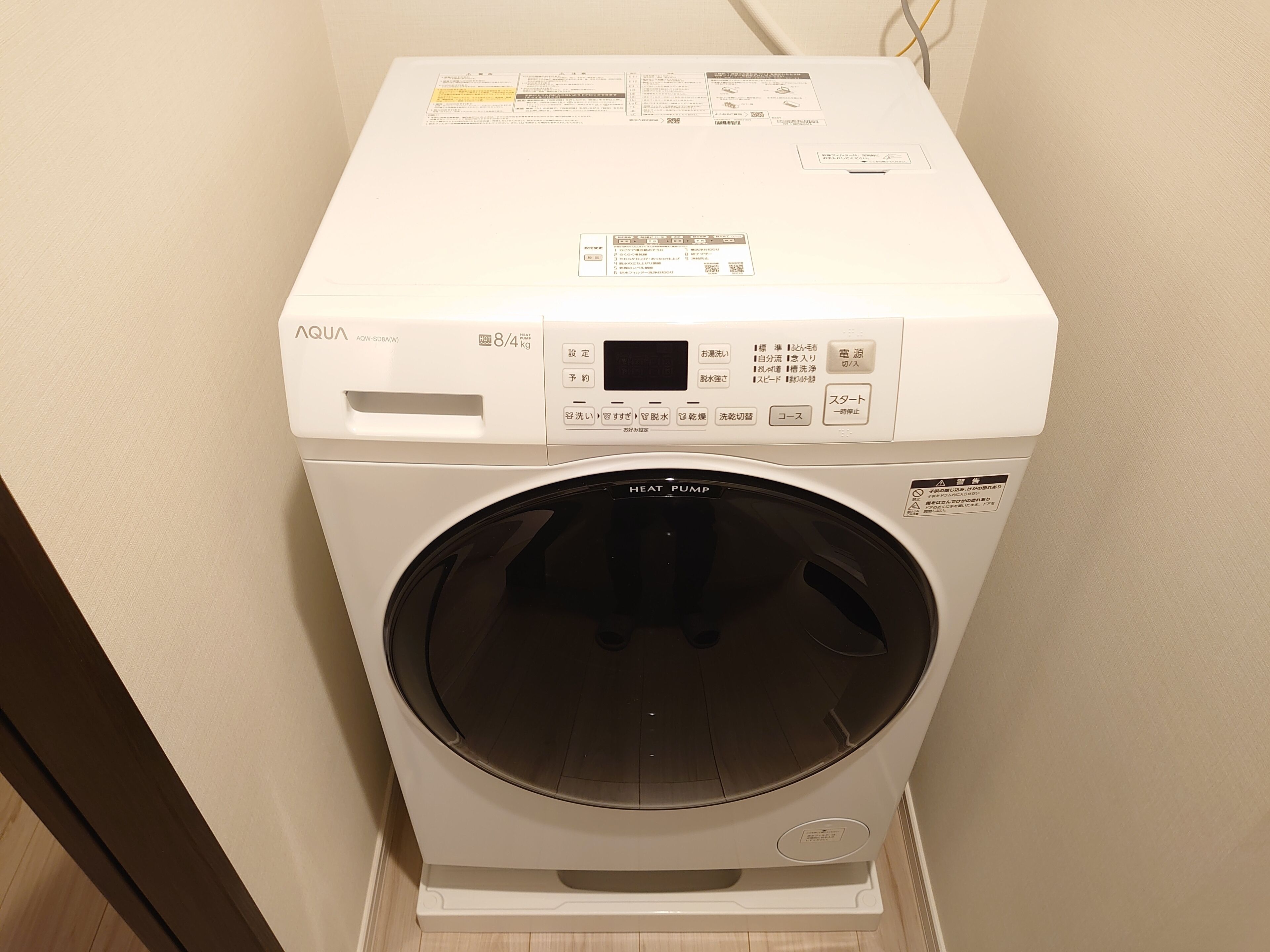 A front-loading washing machine with a control panel, a digital display, and a label indicating it weighs 8.4 kg.