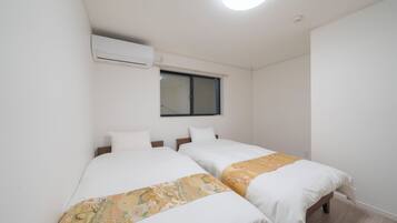 A twin room with two beds, a window with blinds, an air conditioning unit, and a ceiling light.