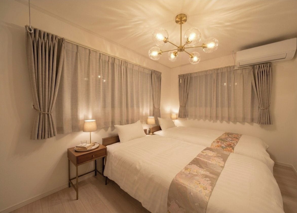 A hotel room with a large bed, two bedside tables with lamps, a chandelier, and curtains.