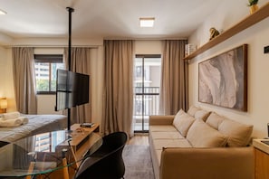 Ein Hotelzimmer mit Bett, einer Sitzecke, einem Fernseher, einem Schreibtisch und einem großen Fenster.