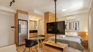A hotel room with a bed, a TV, a desk with a chair, a kitchenette, and a bathroom. - Studio Climatizado a 100m da Esta o Pinheiros (São Paulo)