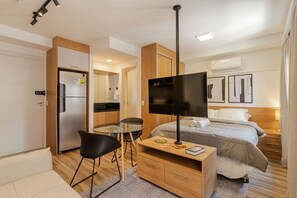 Ein Hotelzimmer mit Bett, Fernseher, Schreibtisch mit Stuhl, einer Küchenzeile und einem Badezimmer.