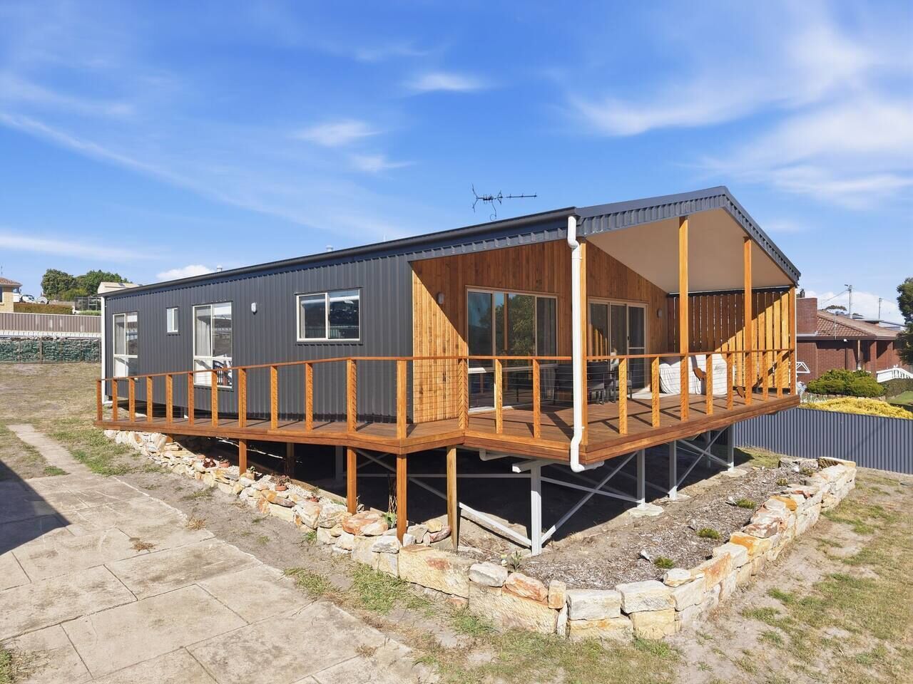 Una cabaña moderna de dos pisos con terraza de madera, ventanas grandes y techo de metal.