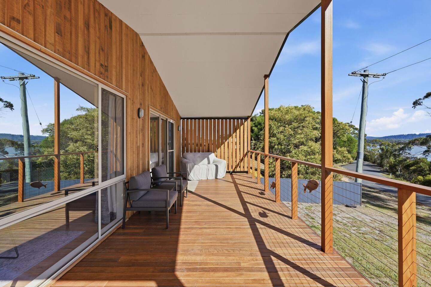 A modern balcony with wooden flooring, glass walls, and a seating area with cushions.