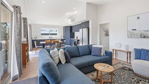 Ein modernes Wohnzimmer mit einer grauen Couch, einem kleinen Holztisch und einem Essbereich mit Tisch und Stühlen.