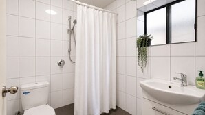 Une salle de bain avec des toilettes, une douche, un lavabo et une plante en pot.