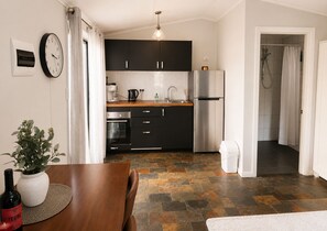 A modern kitchen with black cabinets, a stainless steel refrigerator, and a built-in oven. - Private Coastal Studio - King Bed - Courtyard - Fully Detached - Seacliff Beach (Seacliff)