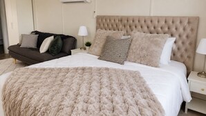 Une chambre à coucher avec un grand lit, un canapé, une table de chevet et un climatiseur fixé au mur.