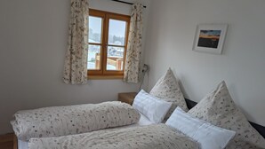 Une chambre avec un lit, une fenêtre avec des rideaux, une lampe de chevet et un tableau encadré au mur.
