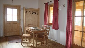 Une table à manger en bois avec des chaises, une porte en bois, une fenêtre avec des rideaux rouges et un porte-manteau.
