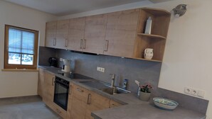 Une cuisine moderne avec des meubles en bois, un four encastré, un évier en acier inoxydable et une fenêtre avec des stores.