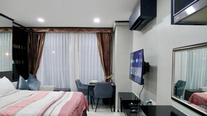 Ett hotellrum med en säng, ett skrivbord, en stol, en tv och en stor spegel.