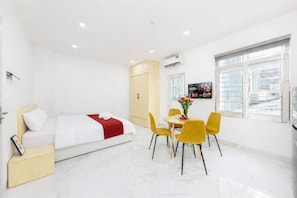A modern hotel room with a bed, a dining table with chairs, a TV, and a window with a city view. - Collection O Ba Dinh - Japanese Town (Hanoi)