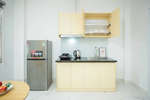 A compact kitchen with a stainless steel refrigerator, a wooden cabinet with a microwave, and a small countertop with a kettle. - Collection O Ba Dinh - Japanese Town (Hanoi)